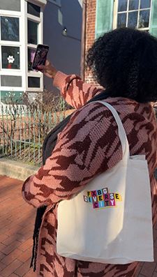 Woman taking selfie on city street holding a diverse city tote bag.