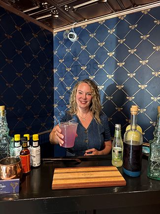 Woman standing behind bar with drink.